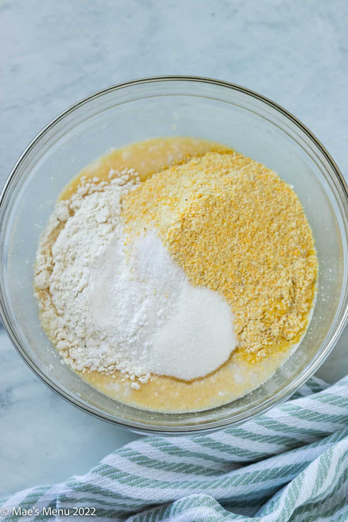 A glass bowl of cornmeal, flour, sugar, and other ingredients for cornbread without milk.