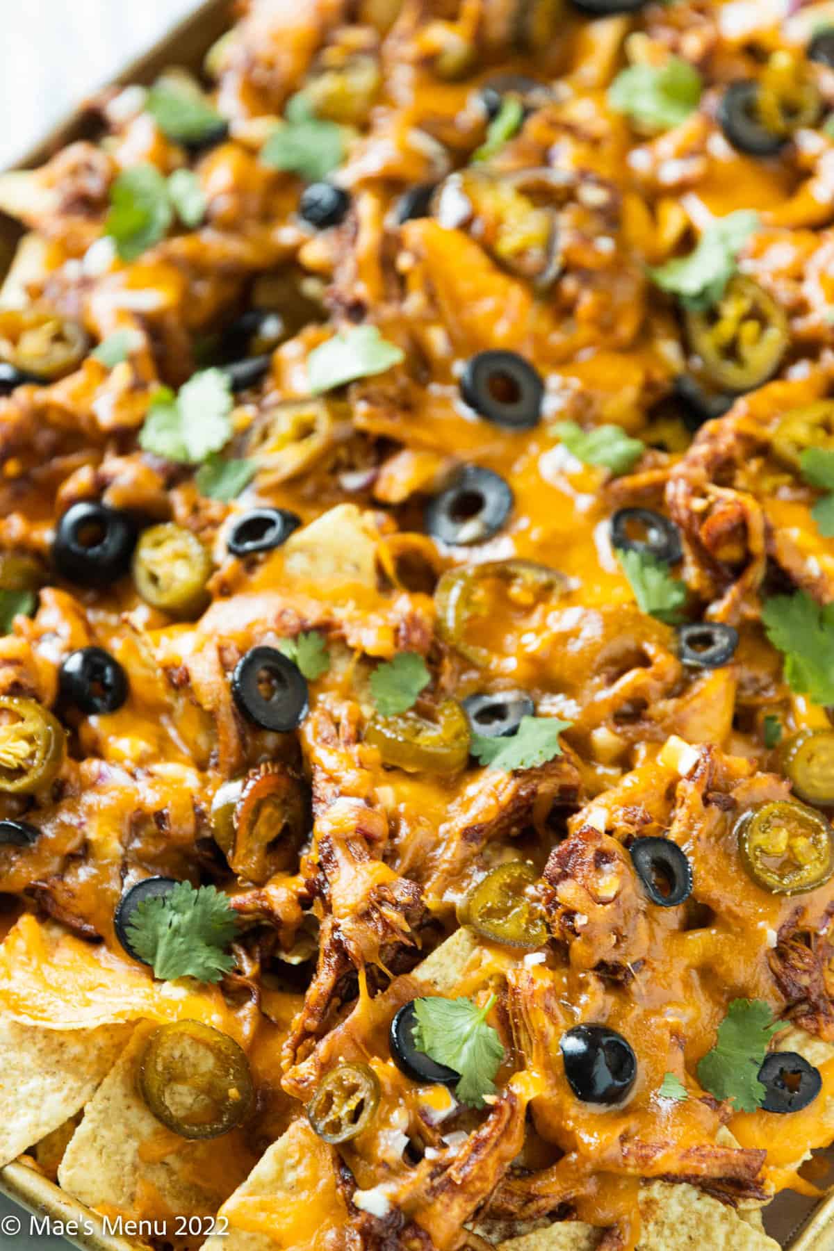 An angled shot of a large sheet pan of barbecue chicken nachos.