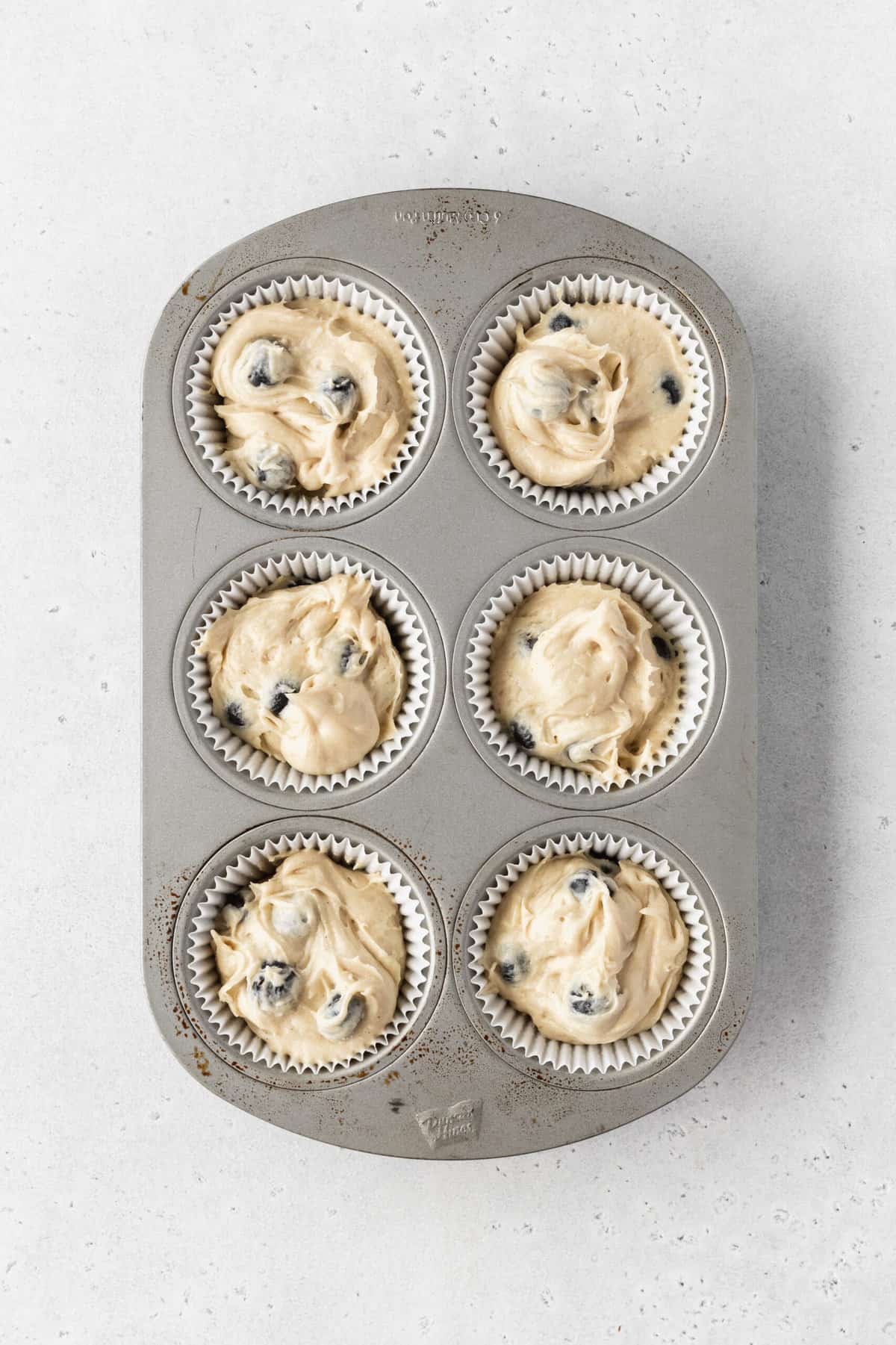 A small cupcake tray with blueberry muffins before baking.
