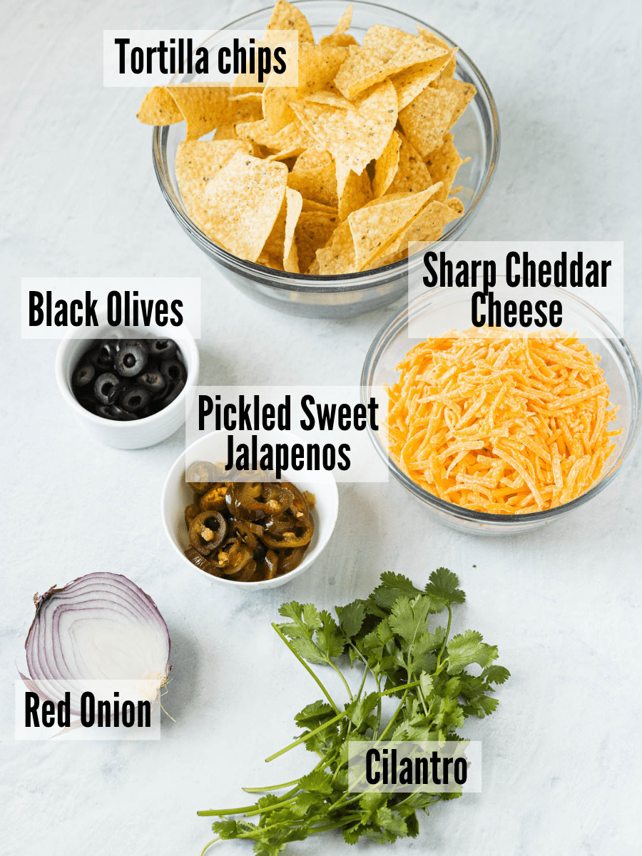 BBQ chicken nachos ingredients: tortilla chips, black olives, pickled sweet jalapenos, cheddar cheese, red onion, and cilantro.