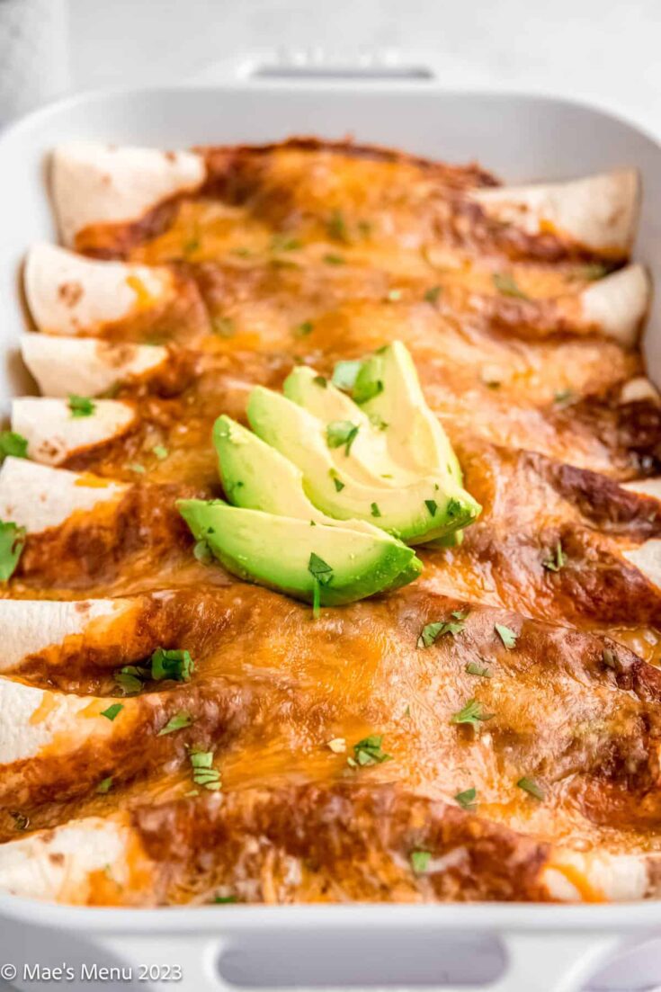 A side shot of a pan of ground turkey enchiladas with sliced avocados on top.
