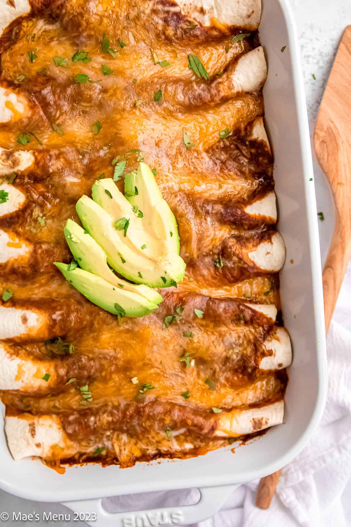An overhead shot of a white dish of ground turkey enchiladas with avocado slices on top.