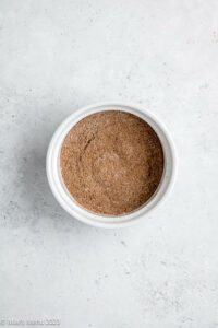 A small ramekin of spices and flour mixed together on a white background.