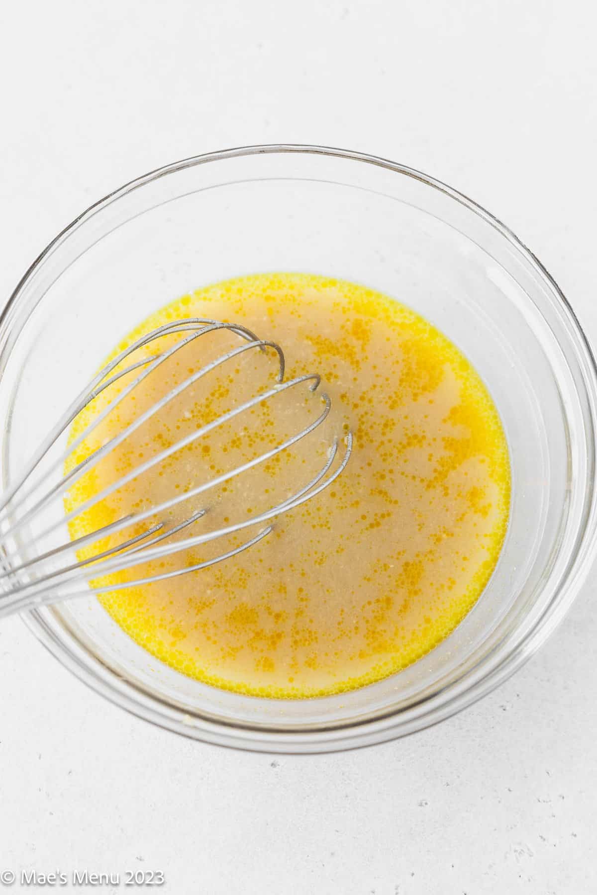 Whisking the miso and water together in a clear bowl on a white background.