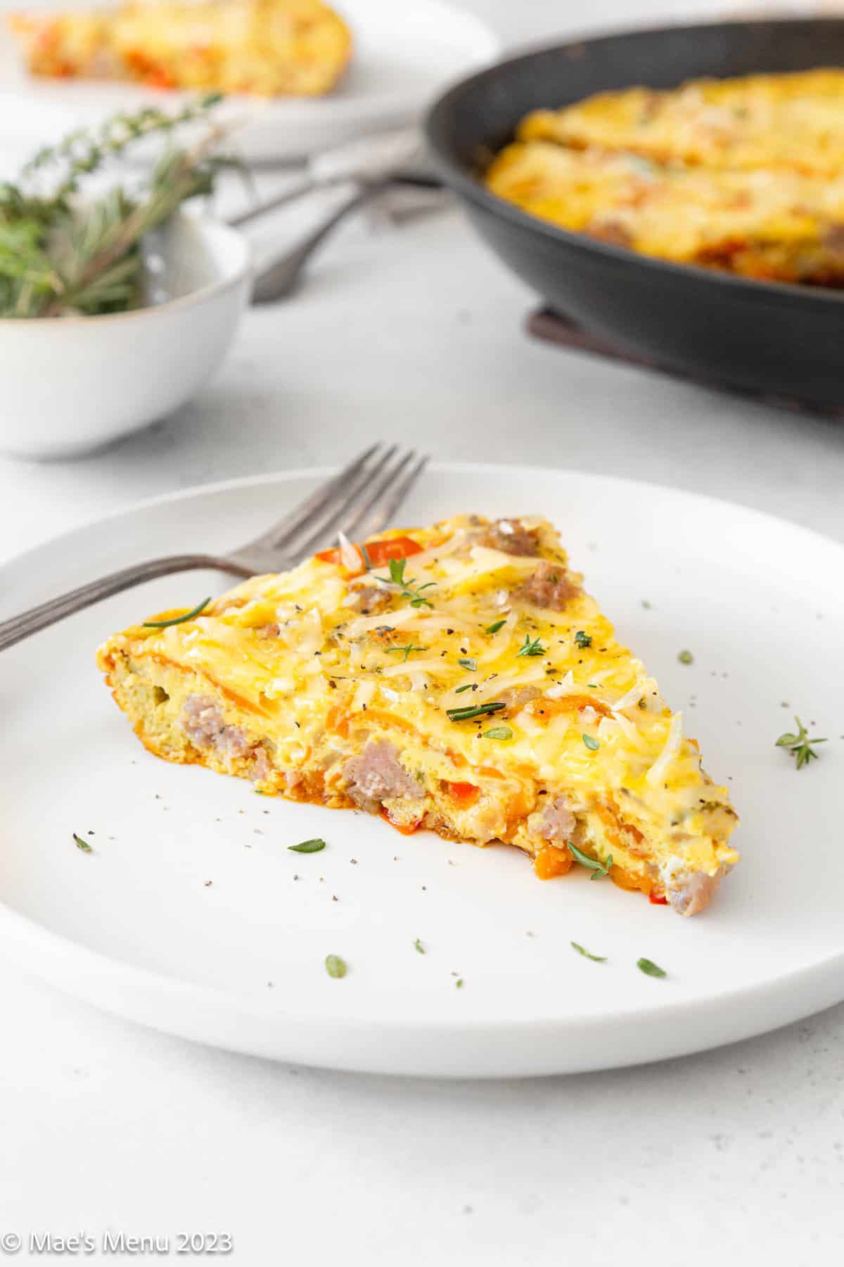 A white plate of sweet potato frittata with the pan of frittata in the background.