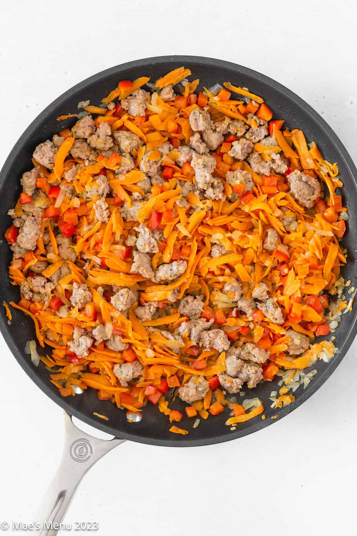 A large skillet of sauteed sausage and shredded sweet potatoes on a white background.