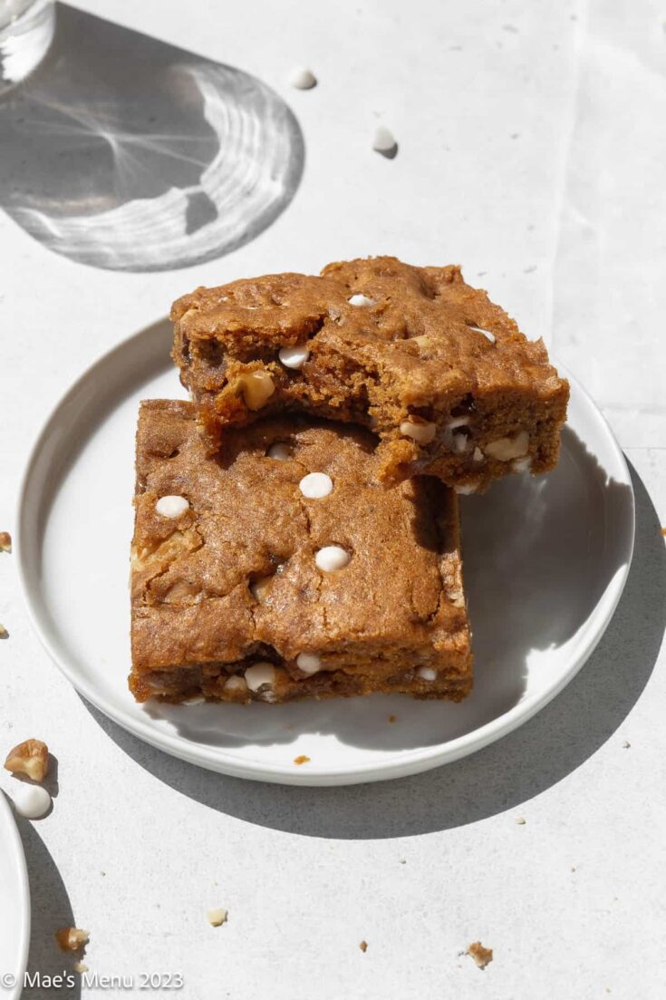 Two vegan blondies on a plate. One has a large bite taken out of it.