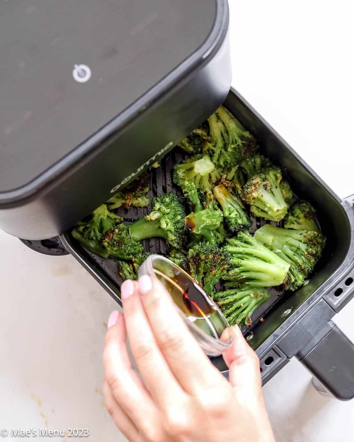 Pouring the balsamic vinegar over the broccoli in the air fryer.
