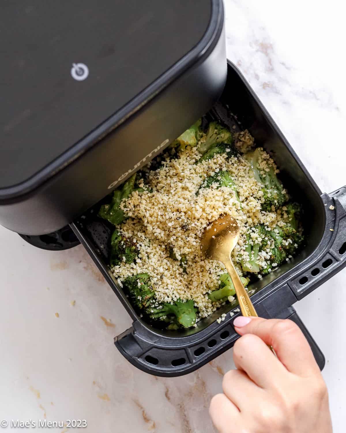 Spooning the breadcrumbs over the broccoli i the air fryer.