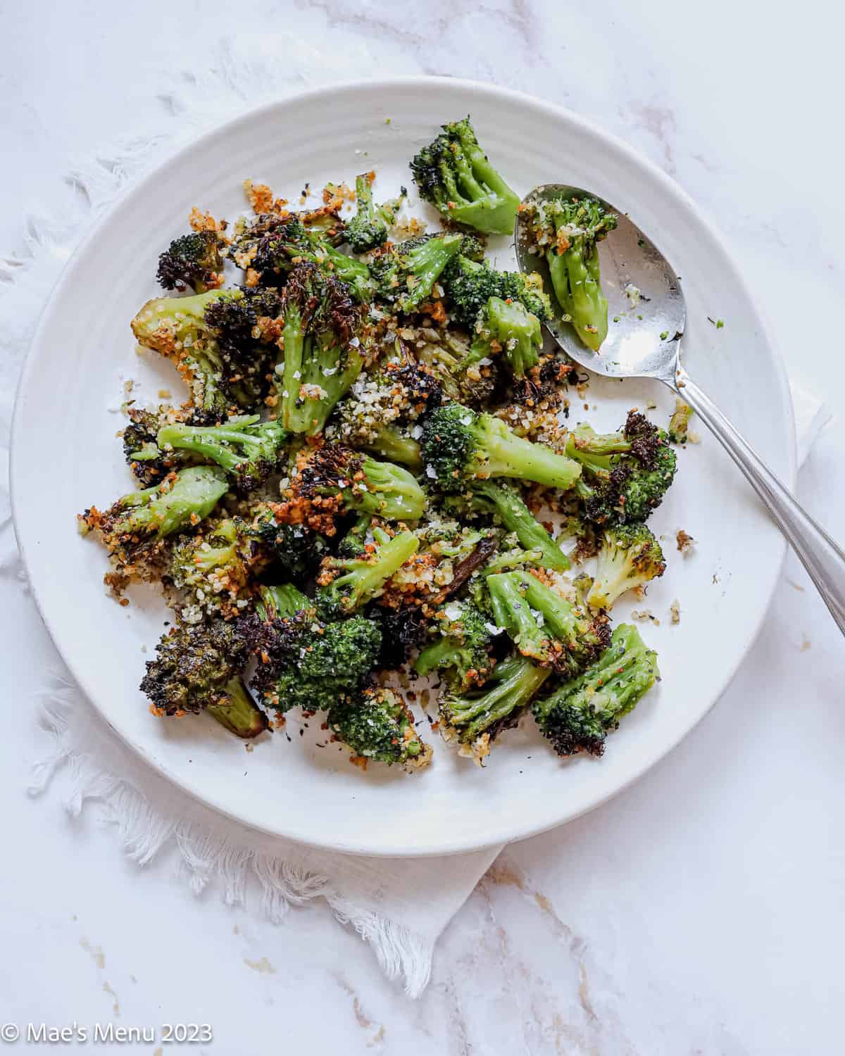 A white plate of frozen air fryer broccoli with a spoon.
