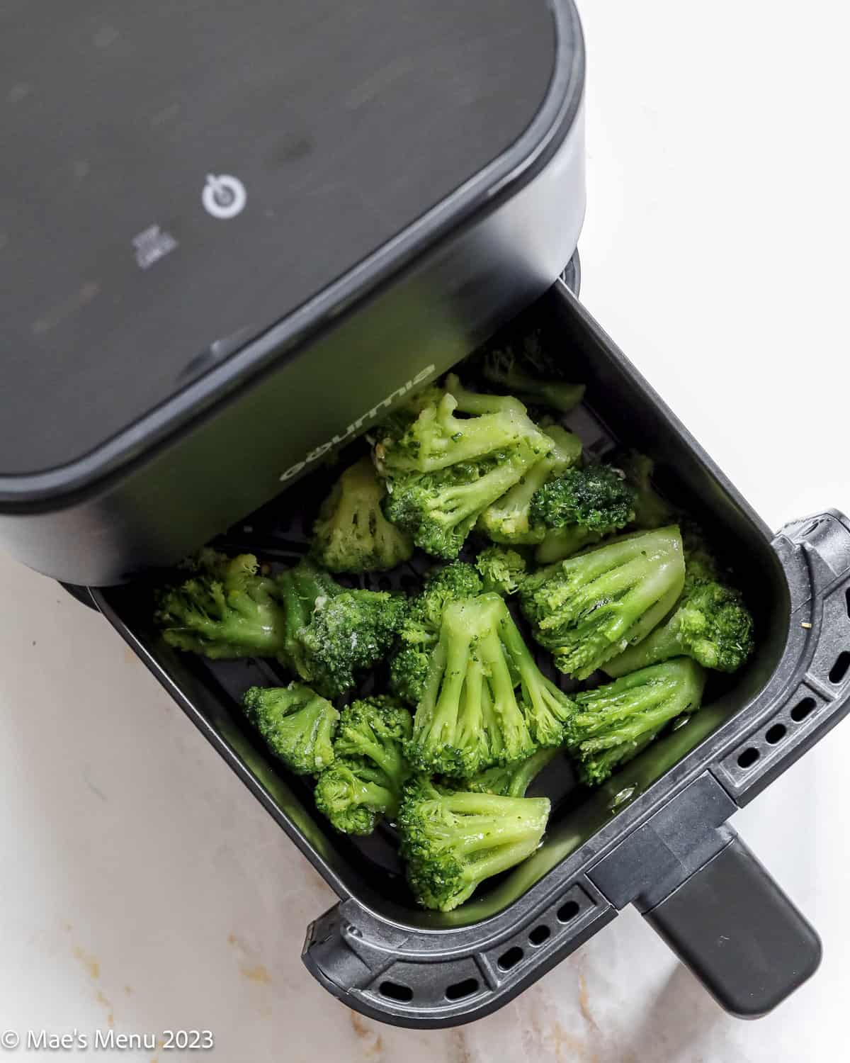 Adding the frozen broccoli to the air fryer.