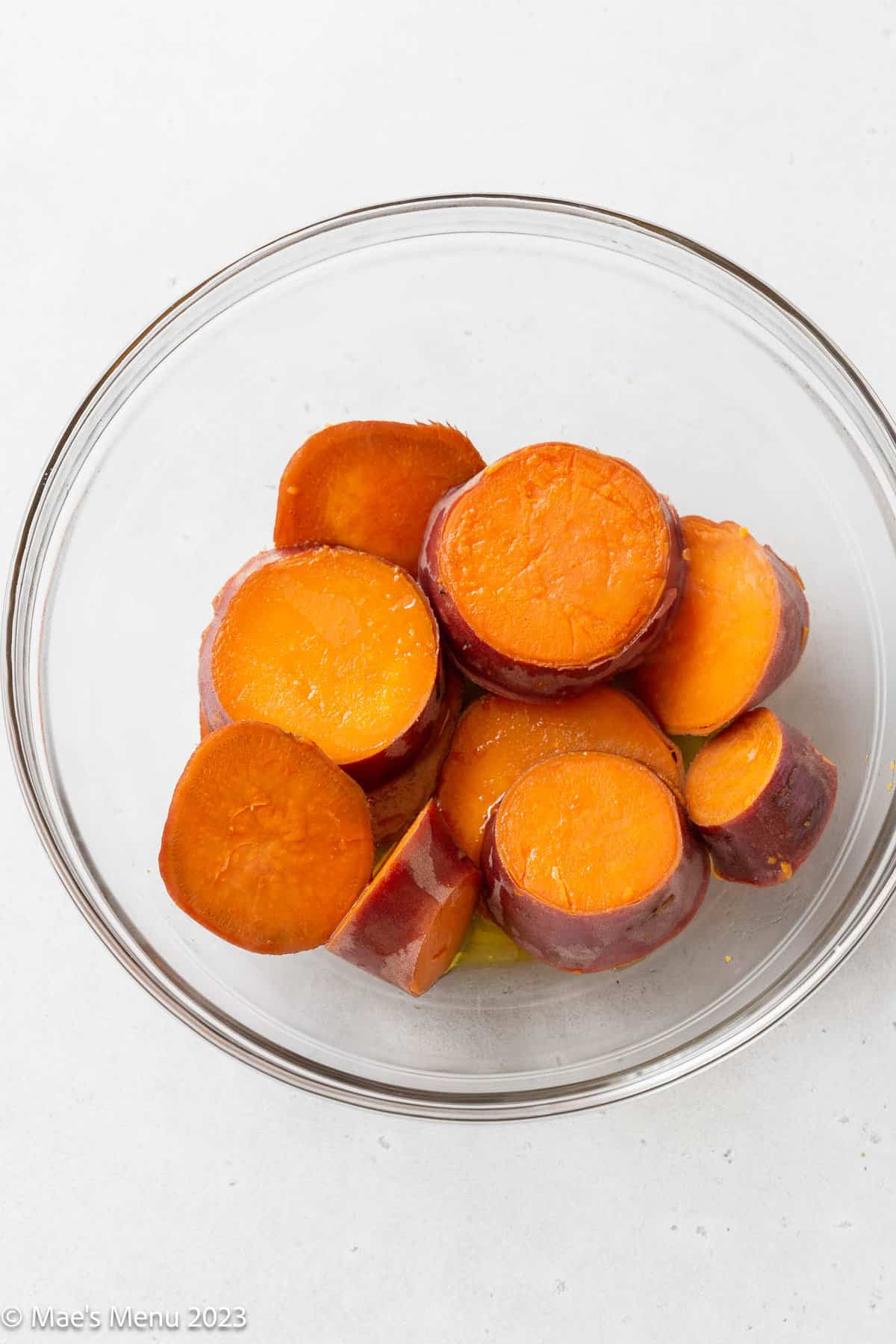 Tossing the boiled sweet potatoes with olive oil in a glass bowl.