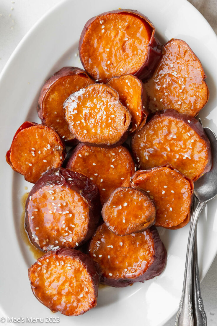 A large white serving plate of crispy roasted sweet potatoes with miso maple glaze and a serving spoon.