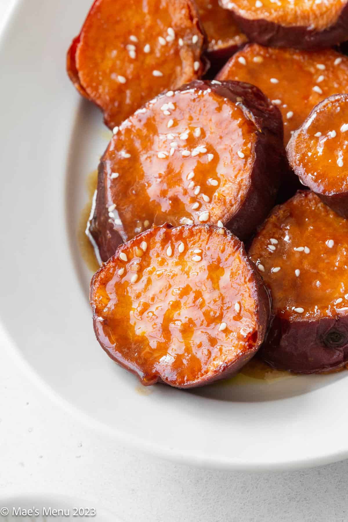 Up-close shot of crispy roasted sweet potatoes with a miso maple glaze on a white plate.