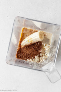 All of the ingredients for a chocolate banana protein smoothie in a blender.