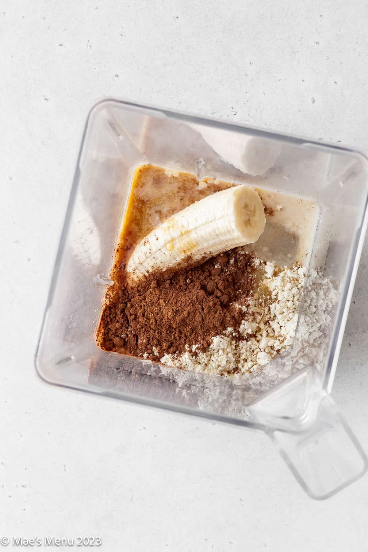 All of the ingredients for a chocolate banana protein smoothie in a blender.