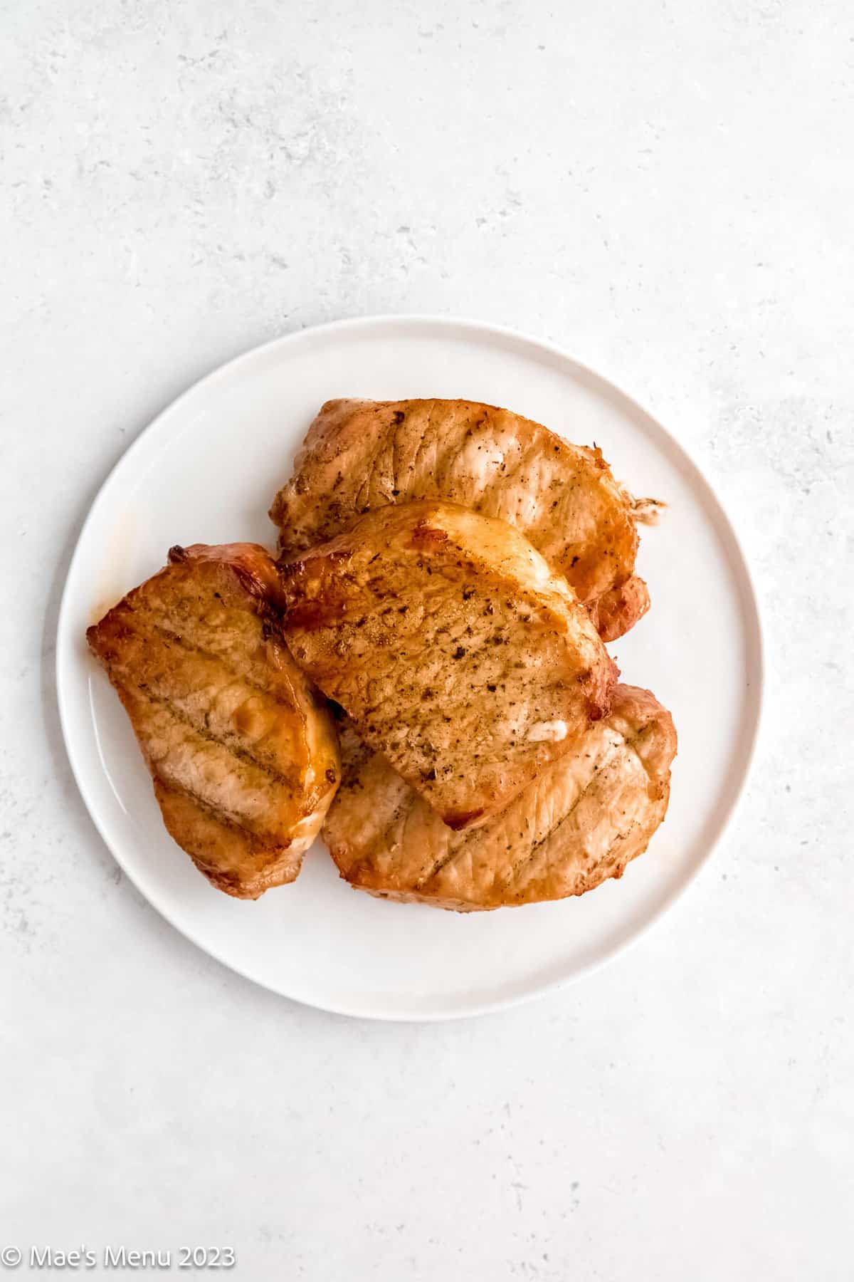 A white plate of grilled pork chops on a white background.