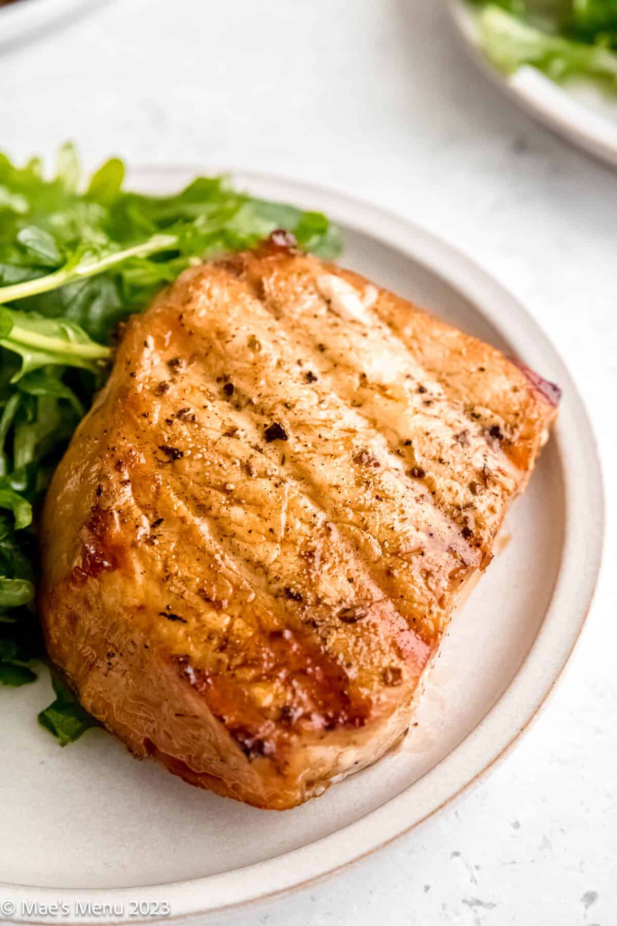 A white plate with grilled pork chops and arugula salad on it.