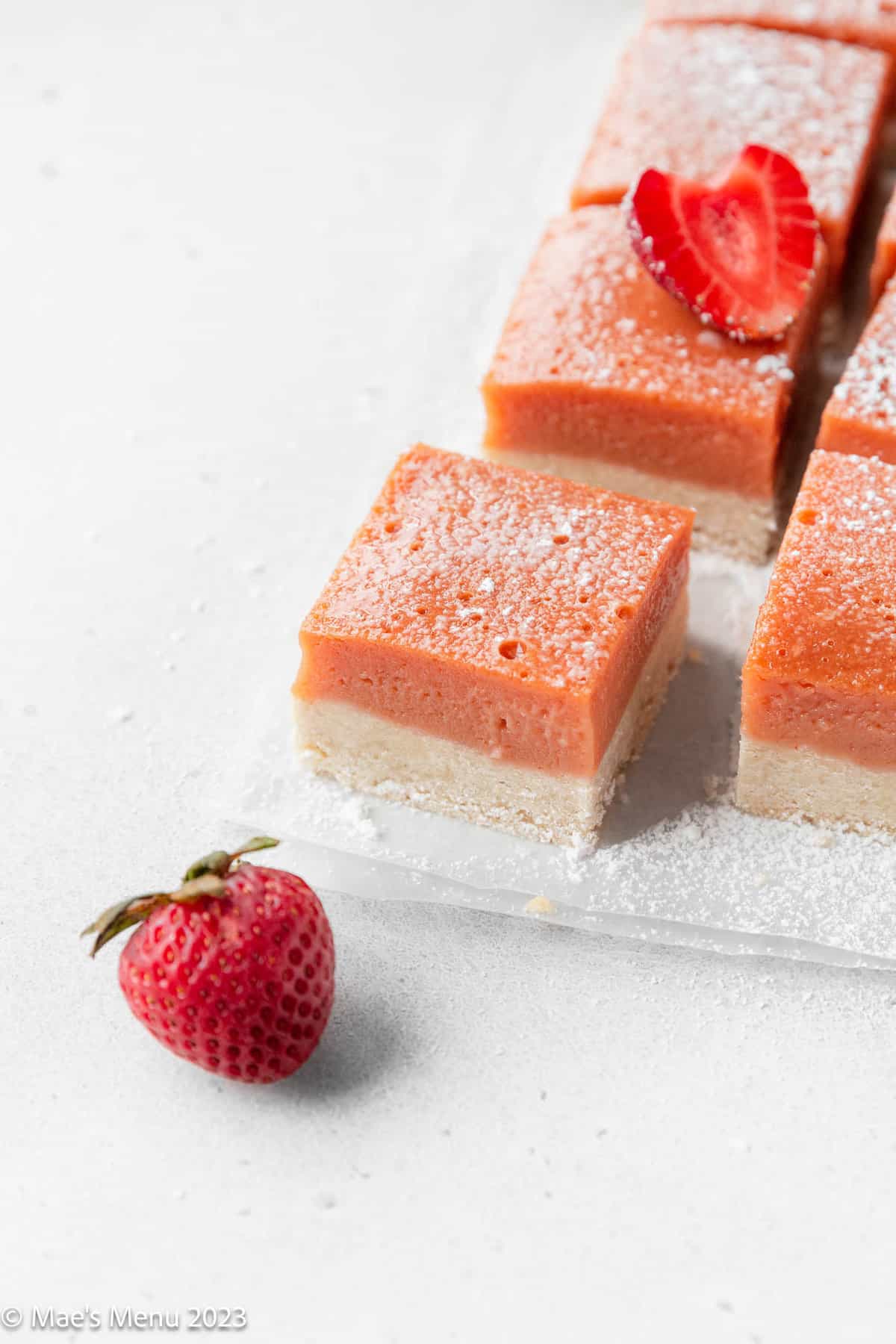Strawberry lemonade bars on the counter with a strawberry.