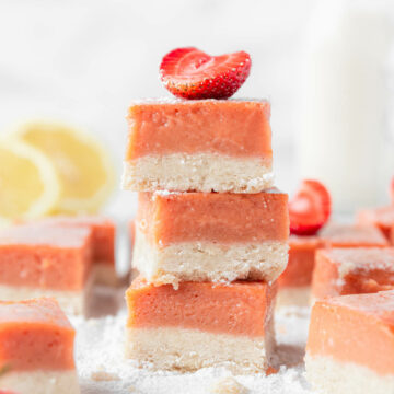 Stacks of strawberry lemonade bars on the counter with lemons, strawberries, and milk.