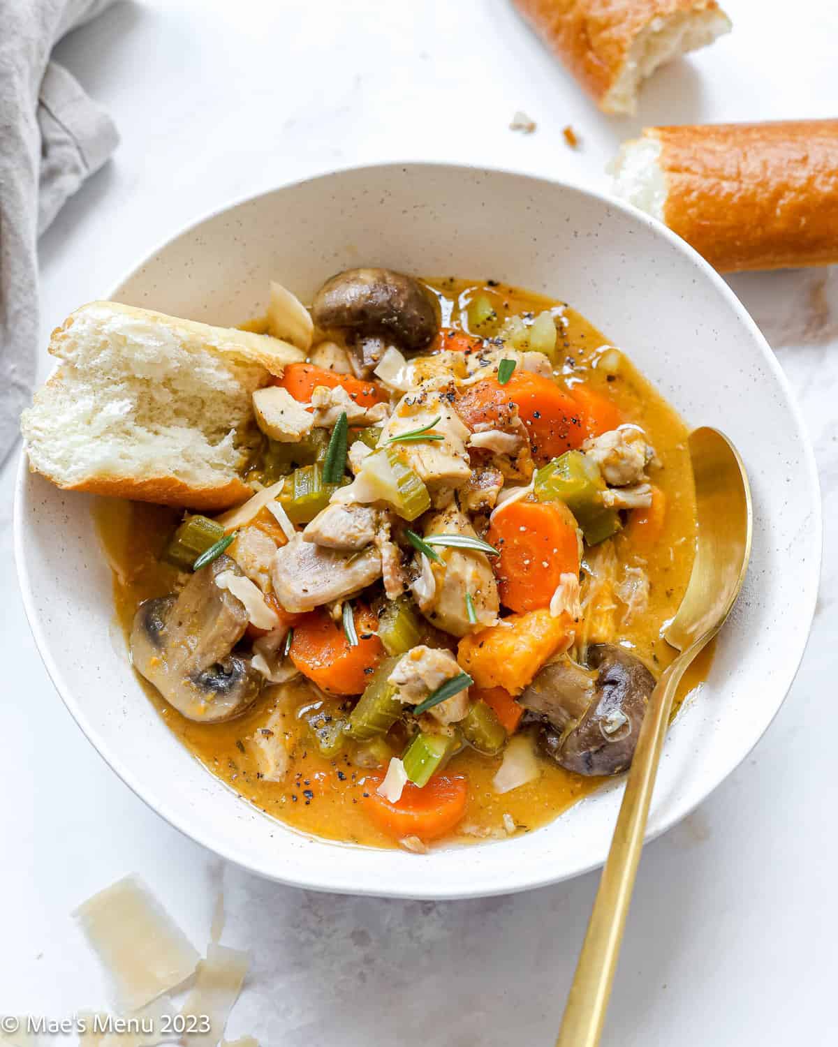 Large white bowl of instant pot chicken stew with bread and a spoon on a countertop.