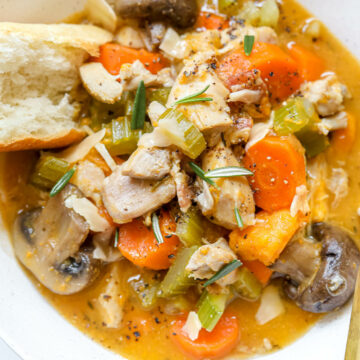 An overhead shot of a white bowl of Instant Pot chicken stew with a piece of bread and a spoon.