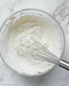 A mixing bowl of freshly whipped cream with a whisk.