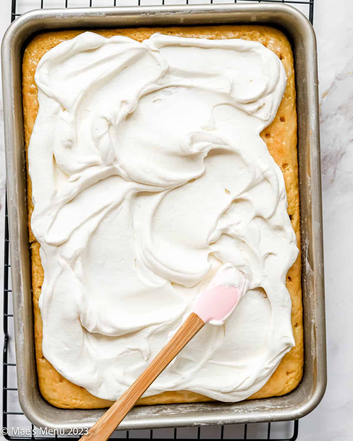A cake pan of frosted lemon poke cake and a frosting spatula.