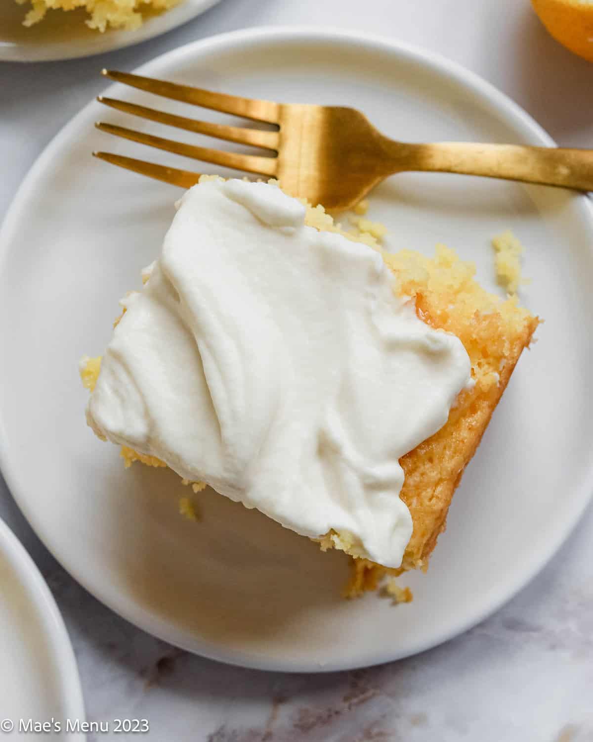 A slice of lemon poke cake on a small white plate with a fork.