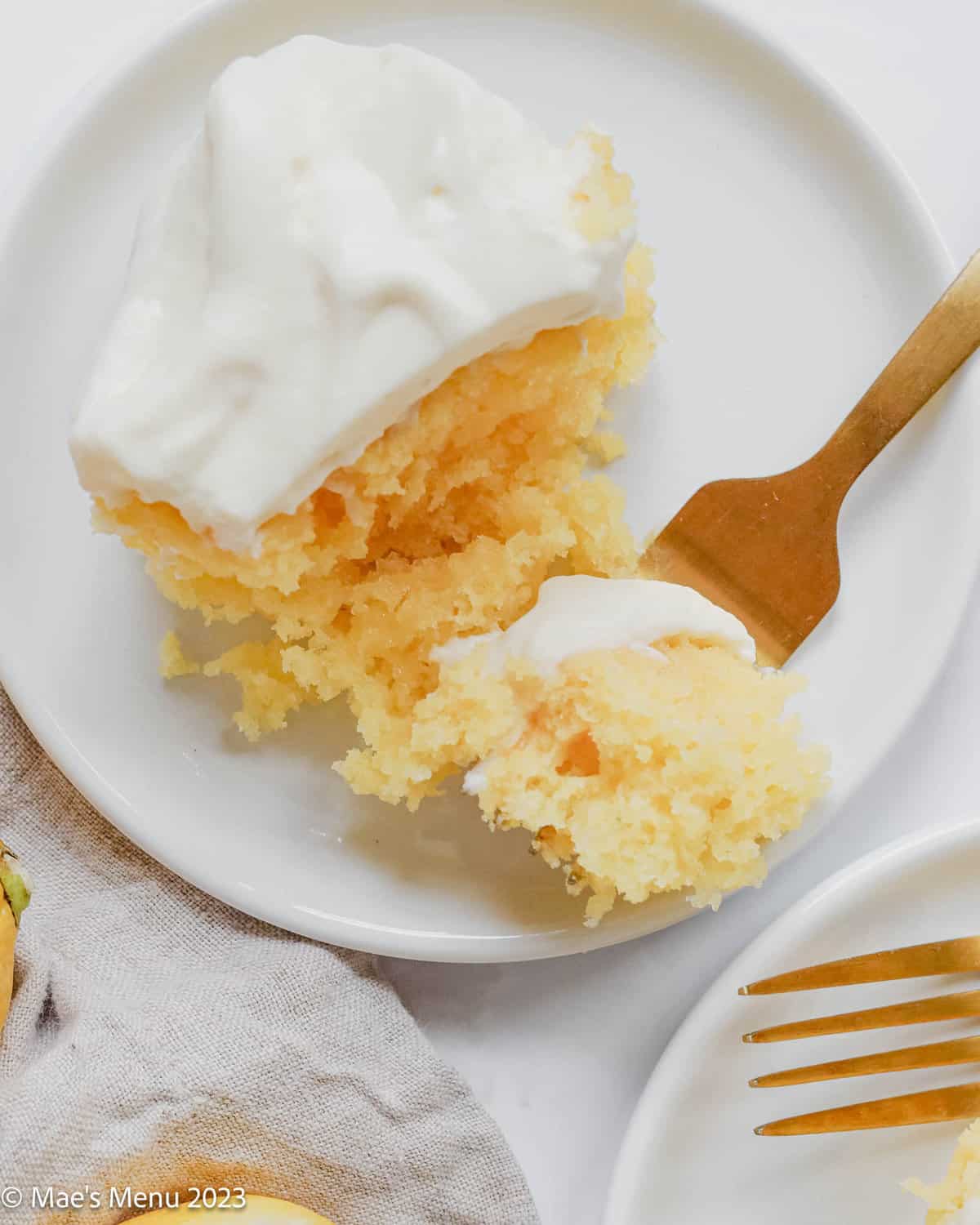 A piece of lemon poke cake on.a white plate with a fork taking a bite out of it.