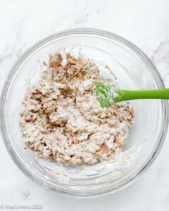 A glass mixing bowl of a flaked tuna and mayonnaise mixture.