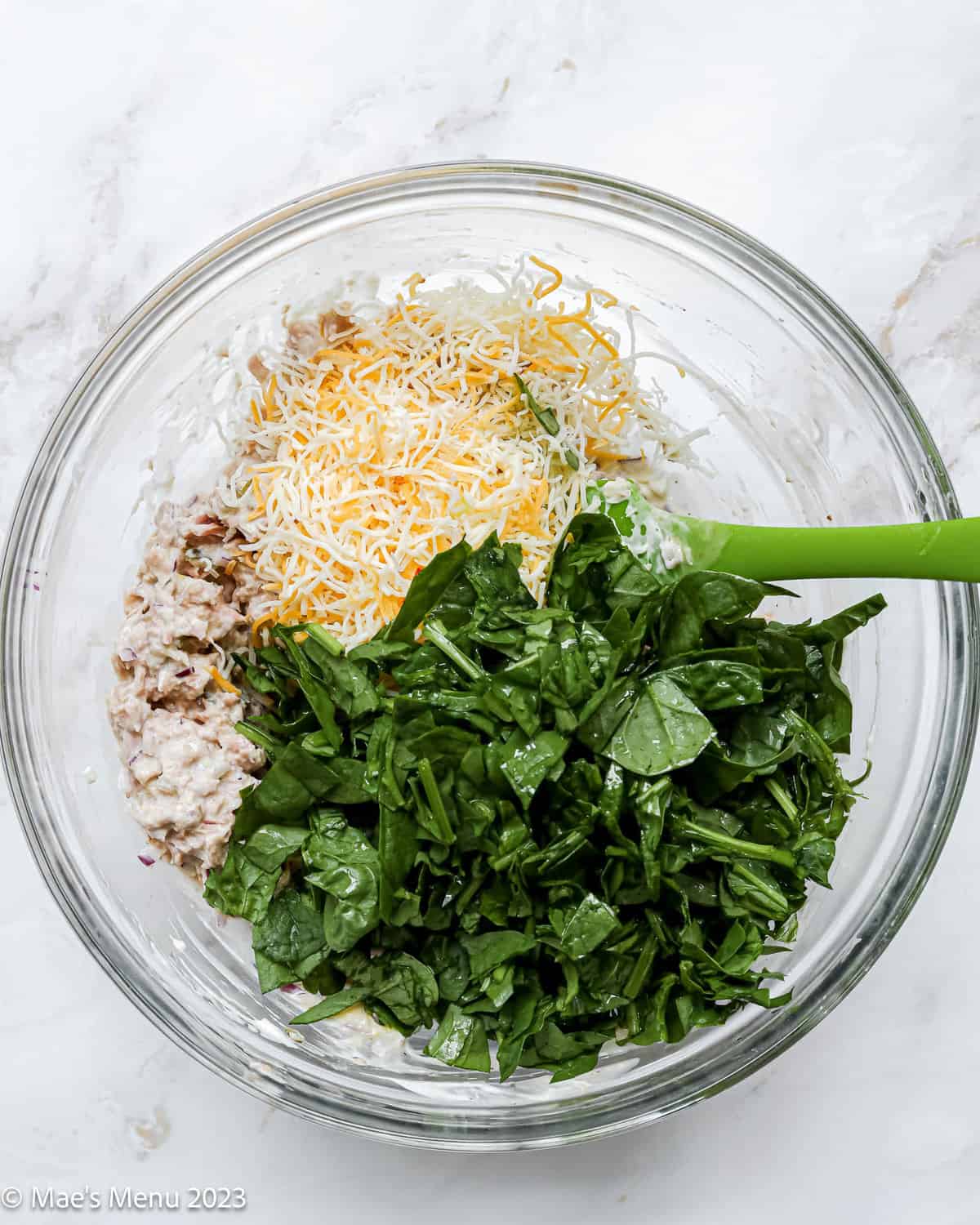 A glass mixing bowl with tuna, cheese, and chopped spinach.