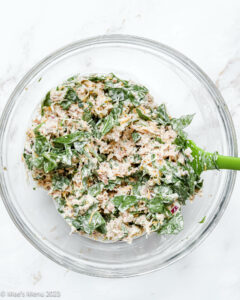 A glass mixing bowl of tuna and chopped spinach.
