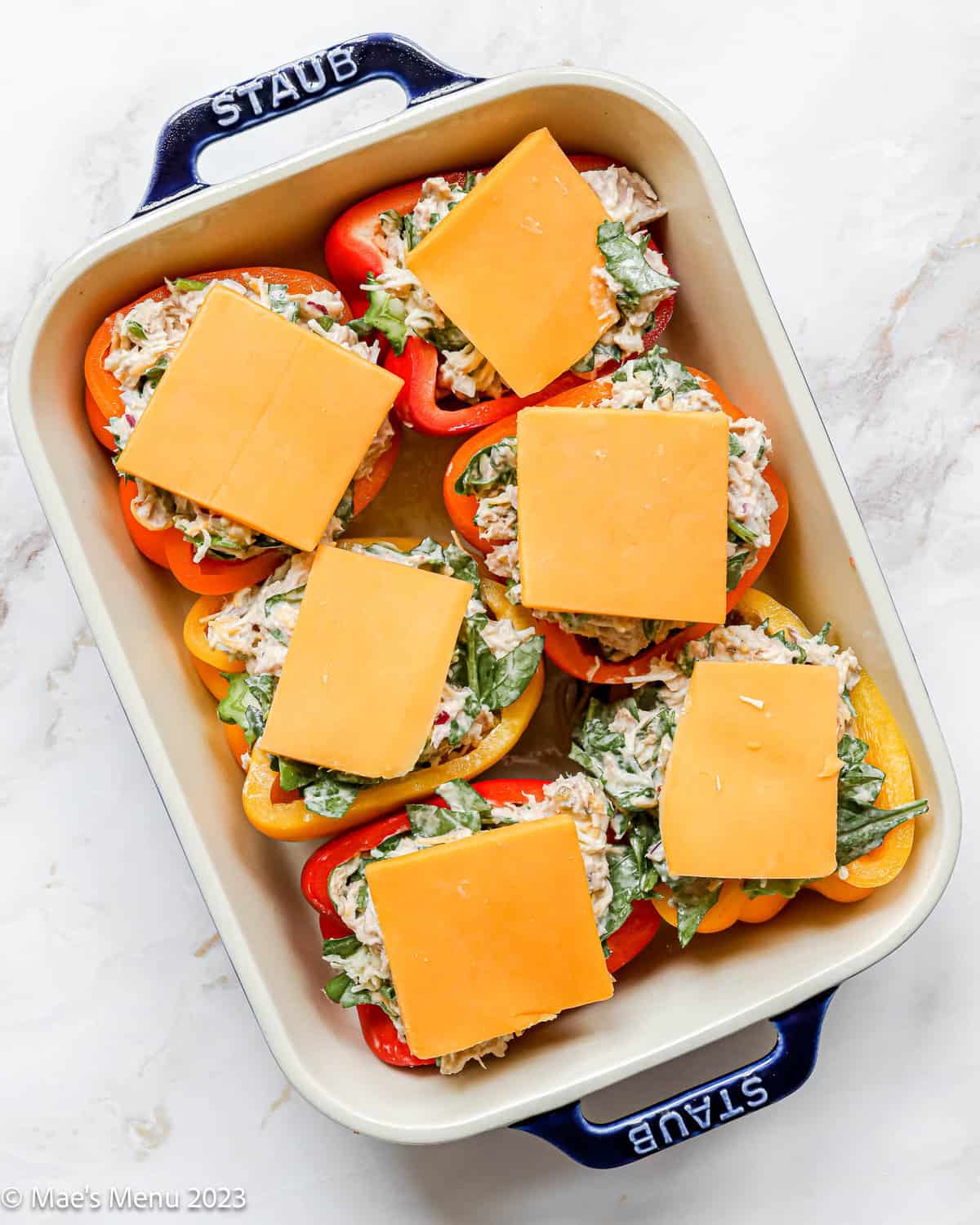A large ceramic pan with tuna stuffed peppers topped with cheddar cheese before baking.