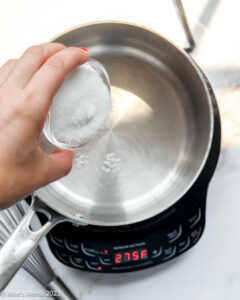 Making simple syrup in a saucepan by adding granulated sugar to the pot of simmering water.