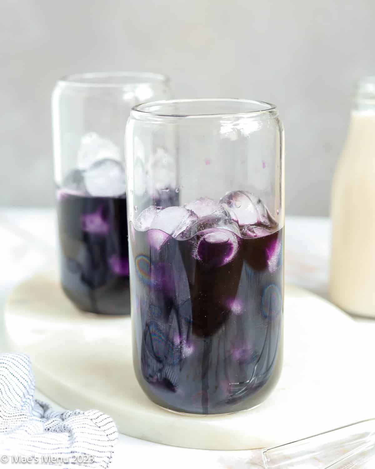 Two glass cups of ube tea with ice cubes.