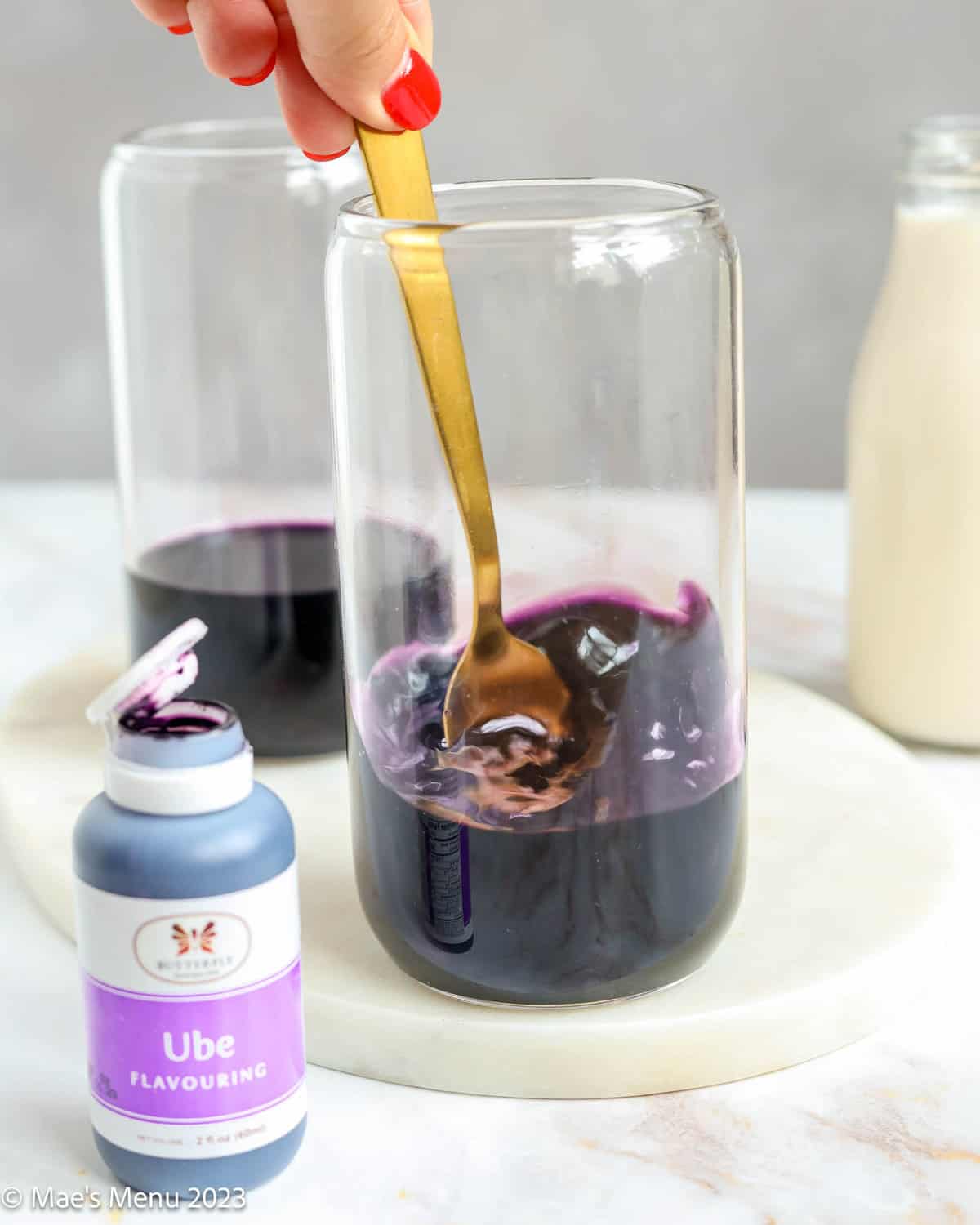 Stirring the ube and tea in the glass cups with a small container of ube flavoring in the foreground.