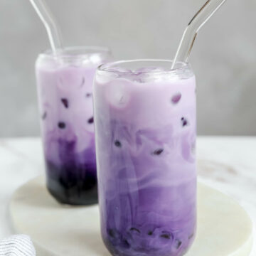 Two glasses of ube boba on a white serving board.