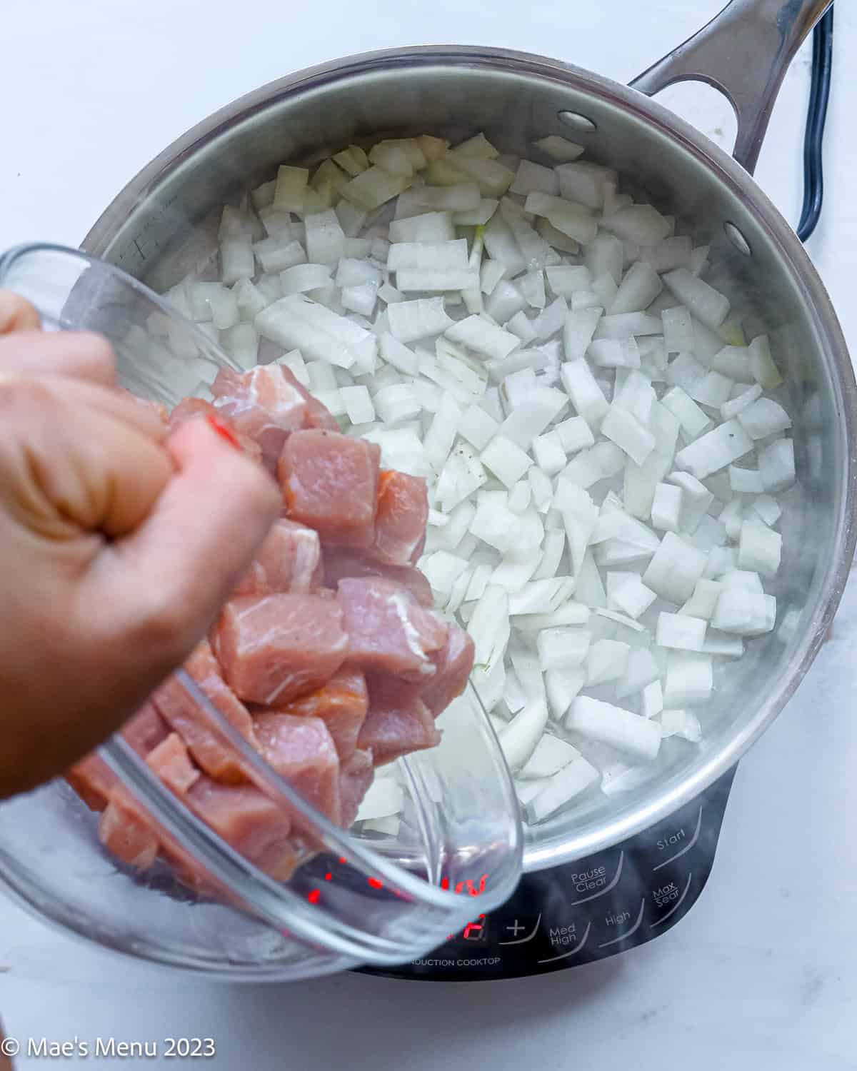 Adding the cubed pork to the sauteing onions.