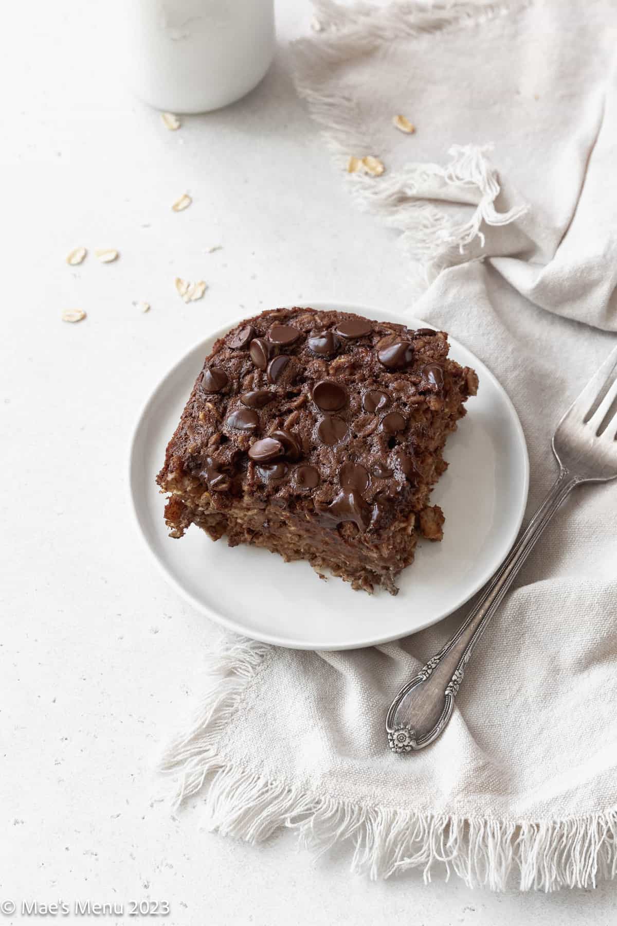 A small white plate with a serving of brownie baked oatmeal on it next to a napkin and fork.