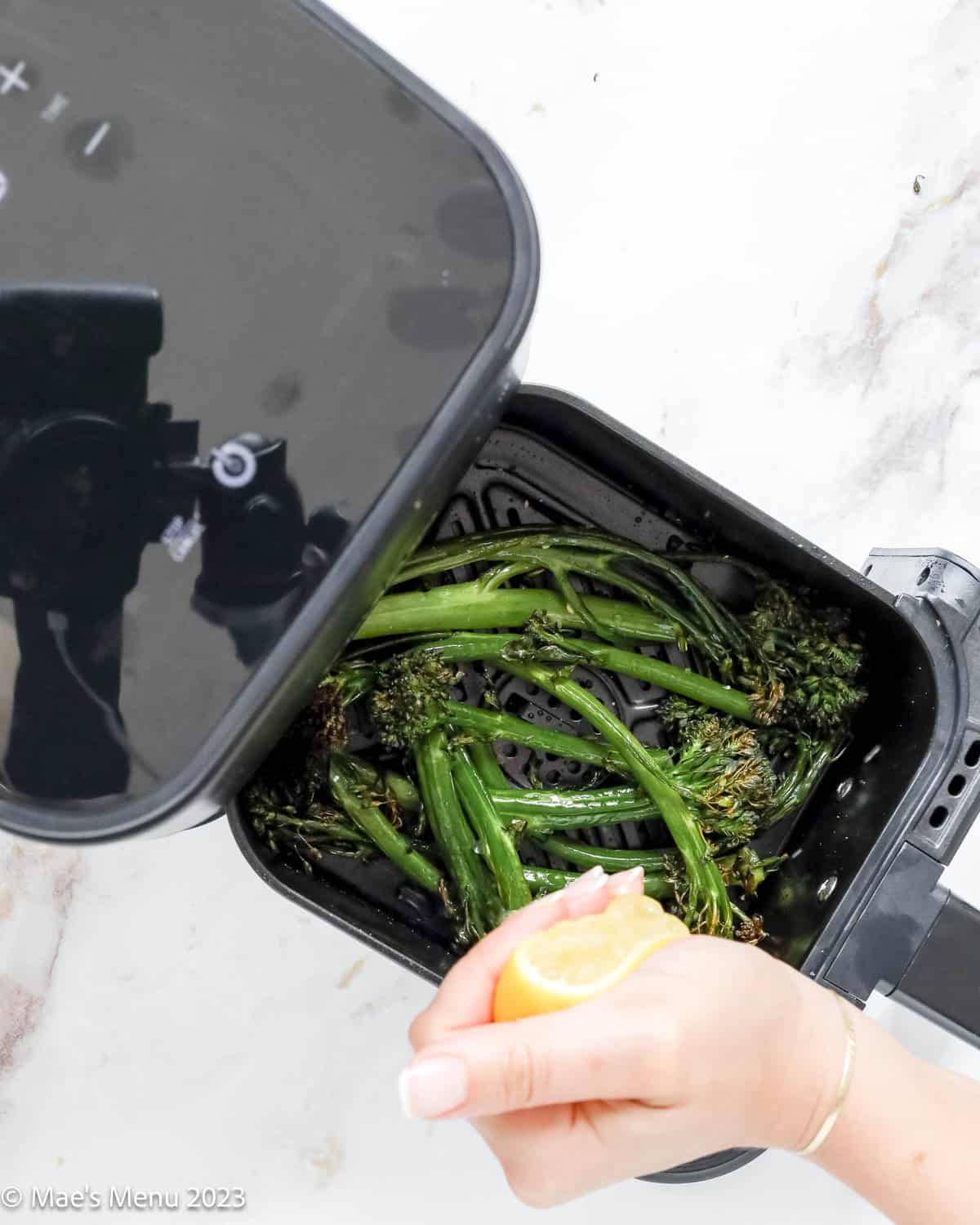 Squeezing lemon over the air fryer broccolini in the air fryer.