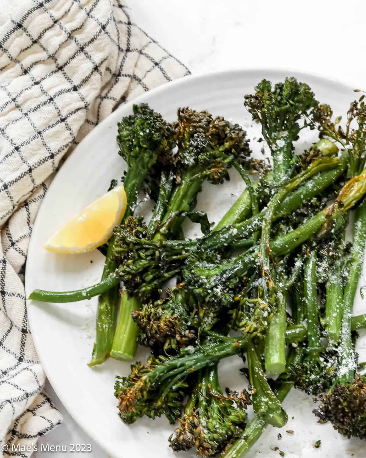 A closeup shot of air fryer broccolini on a white plate with a blue and white napkin.