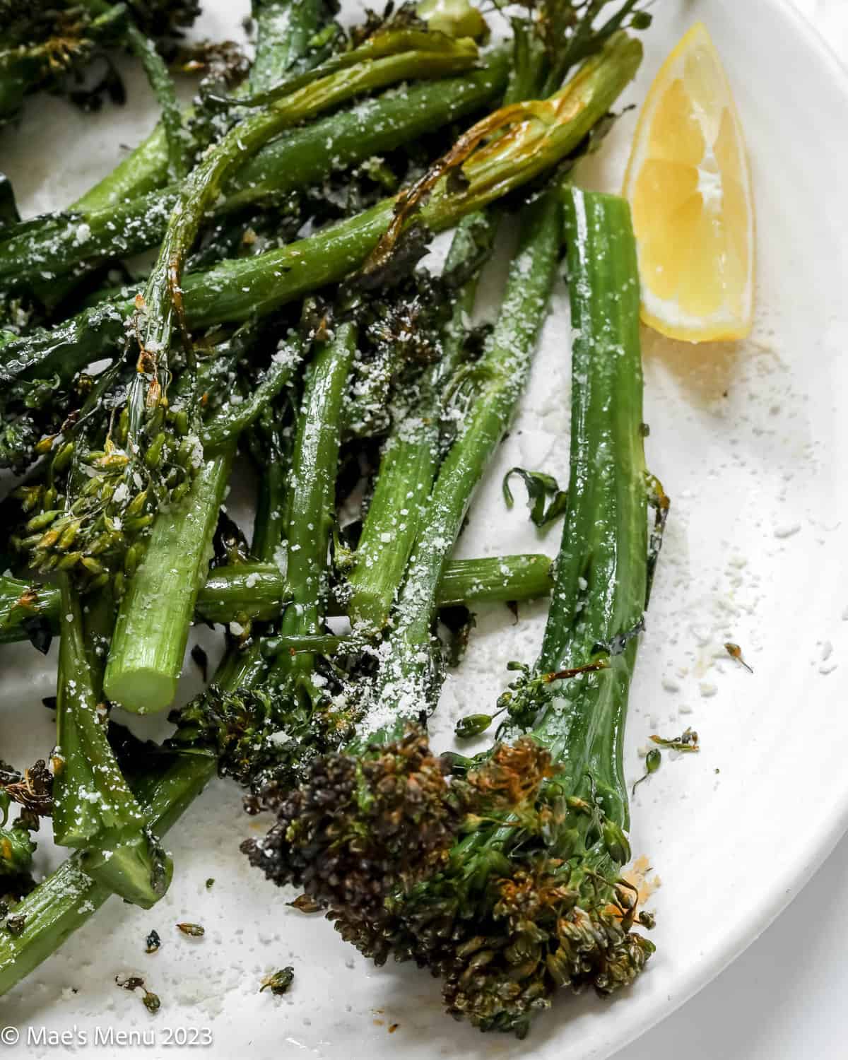 Closeup of air fryer broccolini on a white plate with lemon and parmesan cheese.