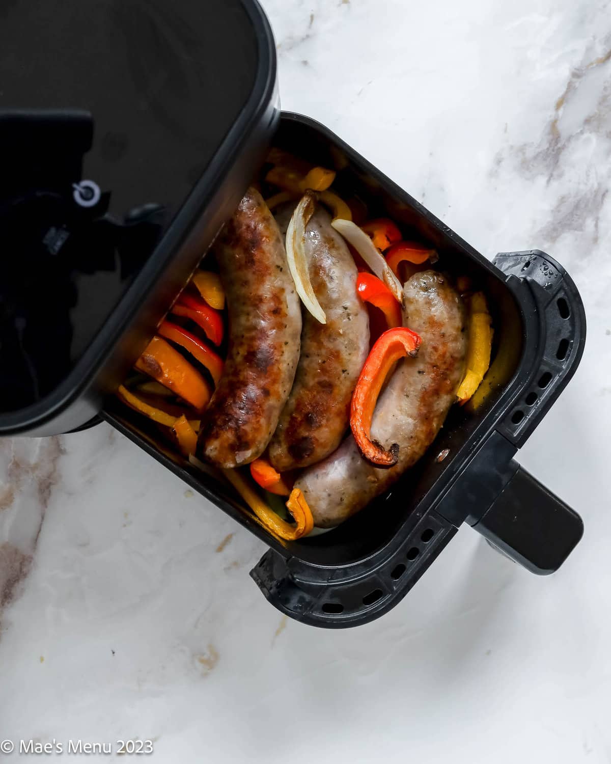 Cooked Italian sausage and peppers in the air fryer basket.