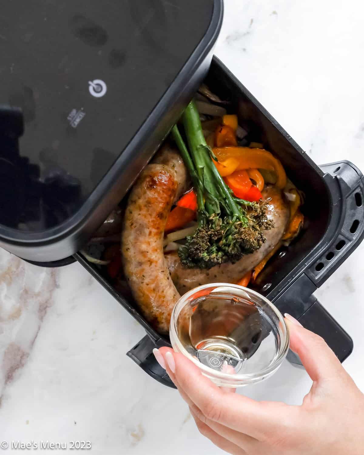 Drizzling the air fryer sausage, peppers, and broccolini, with white wine vinegar.