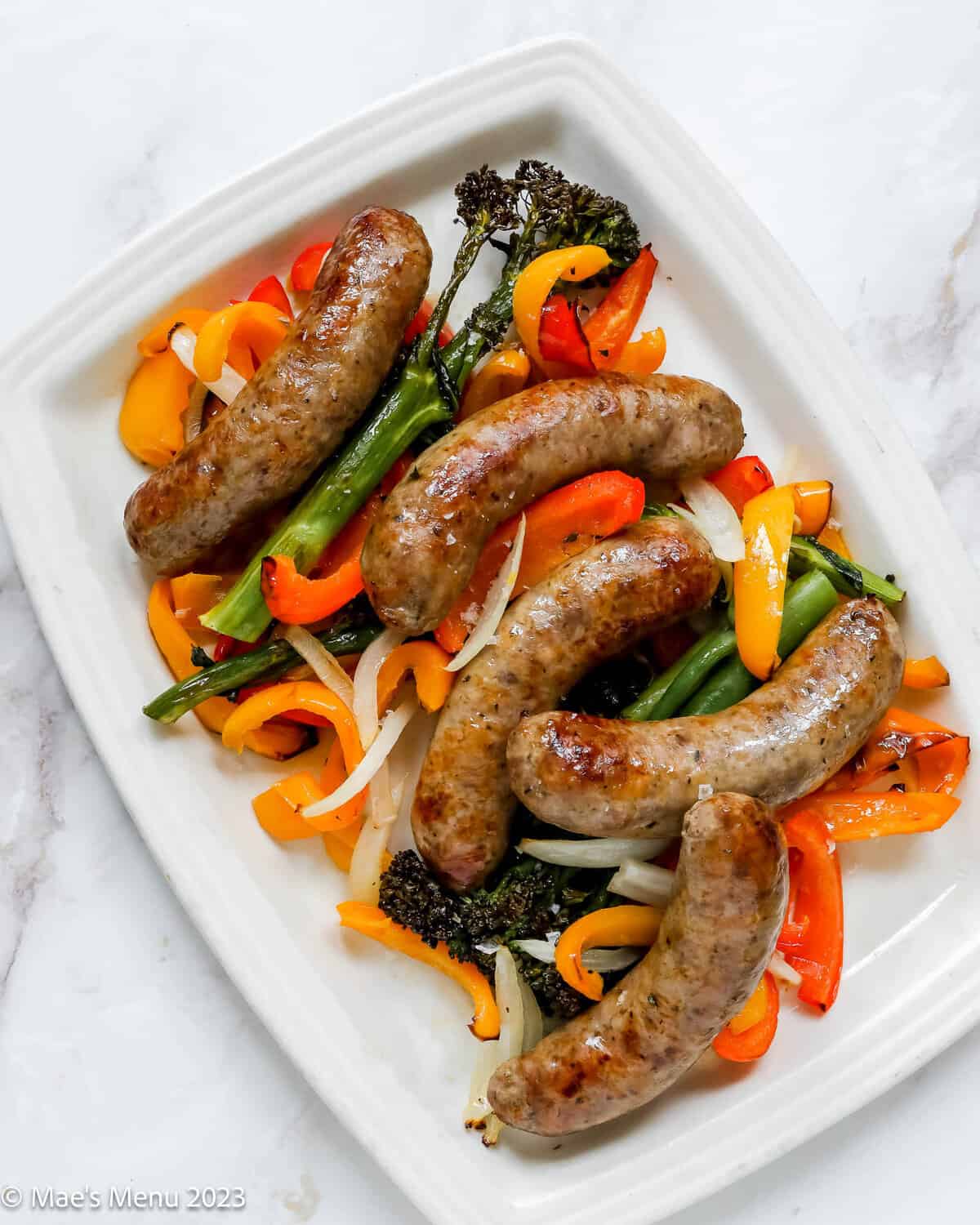 A white serving plate of air fryer Italian sausage with peppers, onions, and broccolini.