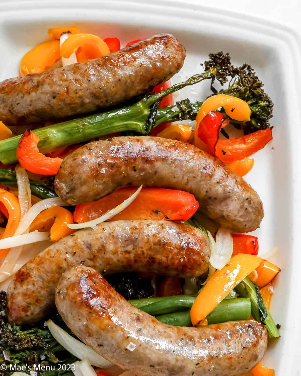 A closeup shot of air fryer Italian sausage, peppers, and broccolini on a white serving plate.