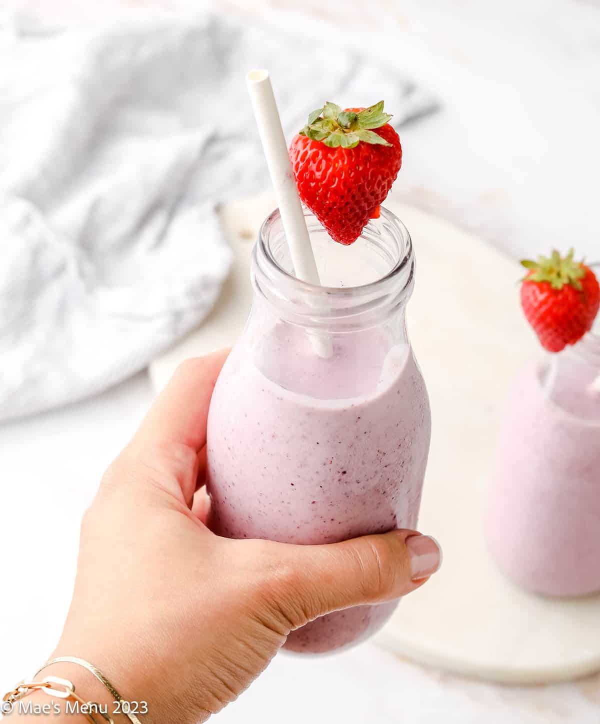 A hand holding a cottage cheese smoothie with a strawberry and a straw.