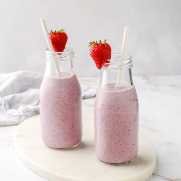 Two cottage cheese smoothies on the counter with strawberries and straws