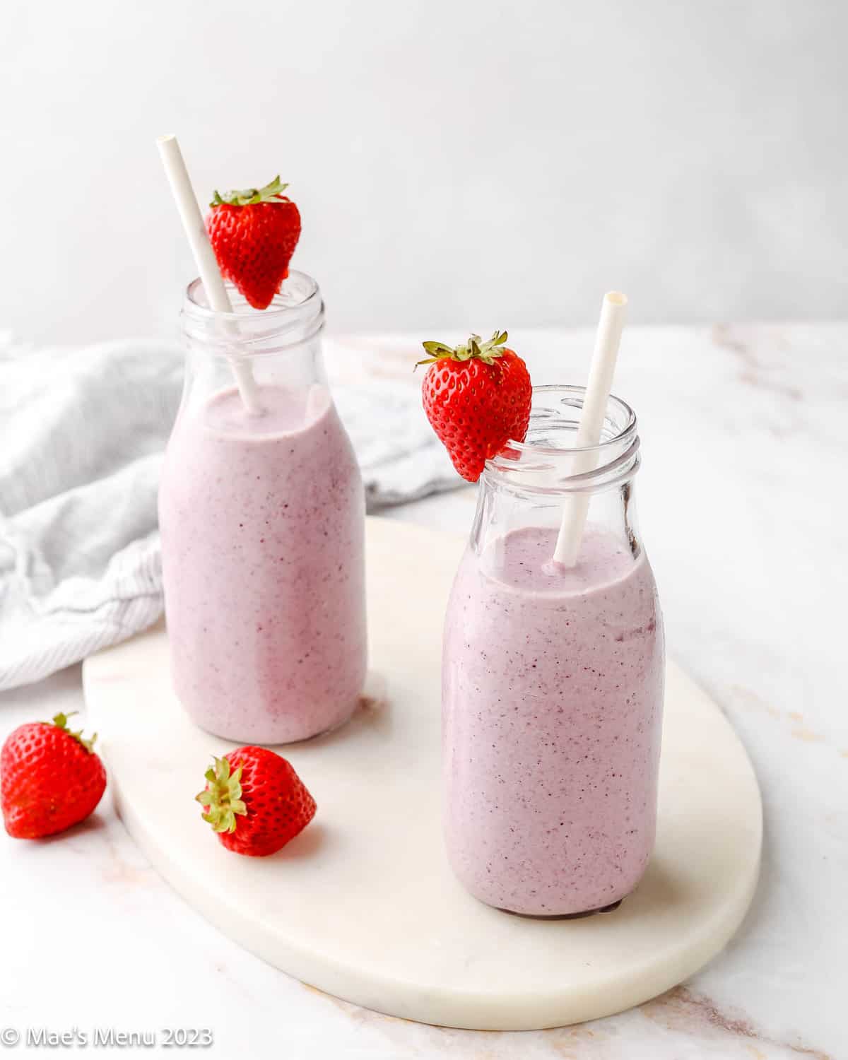 Two cottage cheese smoothies on the counter with strawberries and straws.